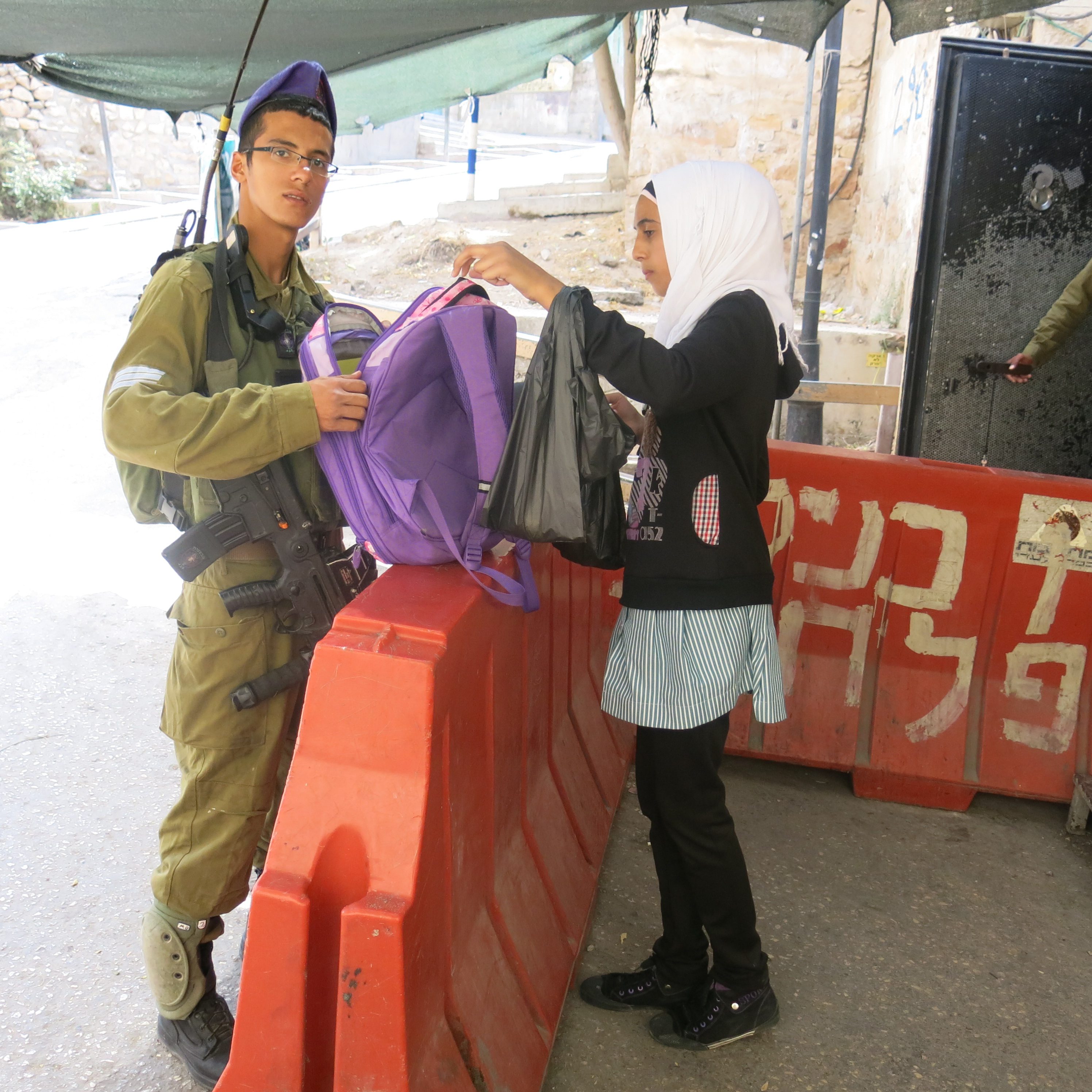 Israelsk soldat tjekker piges skoletaske ved check point i Shuhada Street